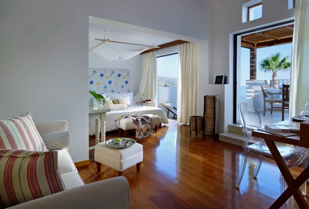 Intérieur d'une Suite Deluxe au St. Nicolas Bay Resort Hotel & Villas montrant les matériaux nobles et l'ouverture sur une terrasse avec pergola.