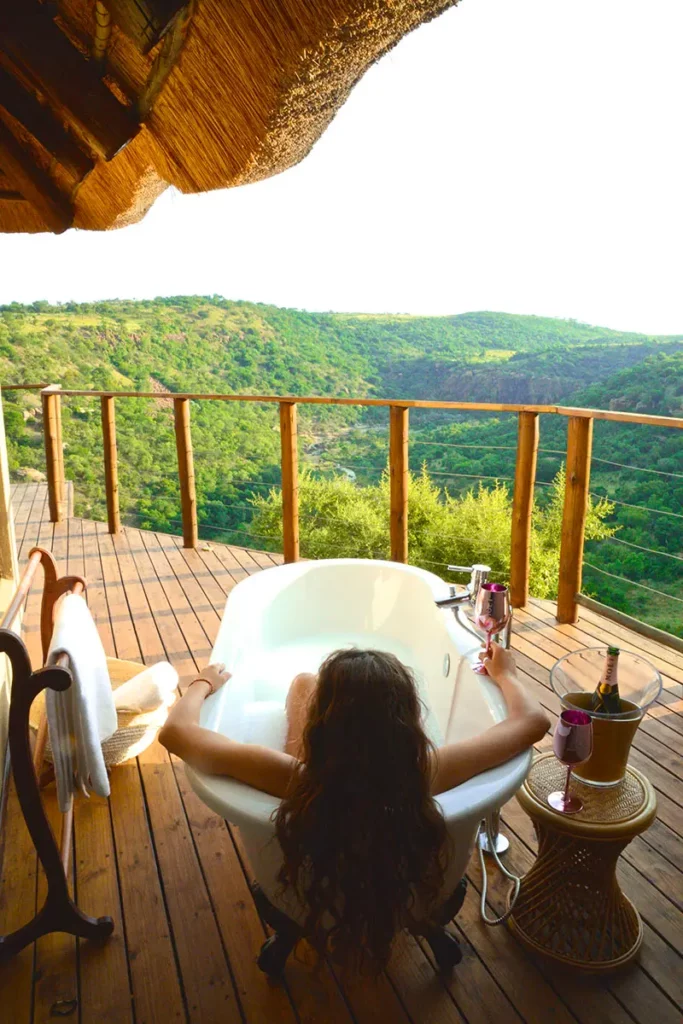 Femme contemplant la savane depuis une baignoire avec du champagne sur la terrasse d'une suite au Esiweni Luxury Safari Lodge.