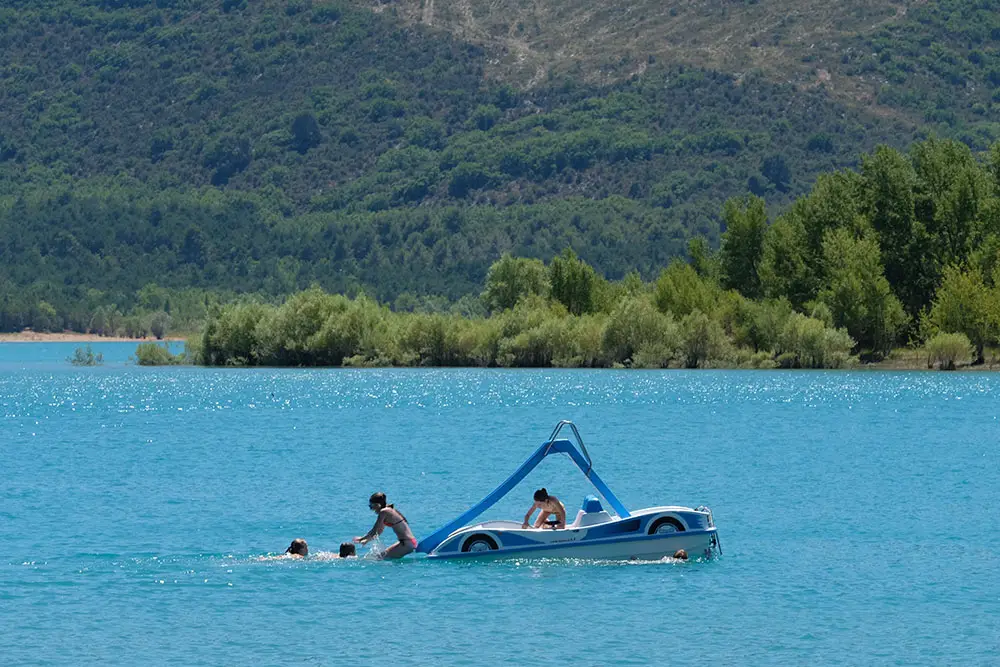 Cinq enfants s'amusent et plongent joyeusement depuis un pédalo toboggan au milieu des eaux turquoise du lac de Sainte-Croix.