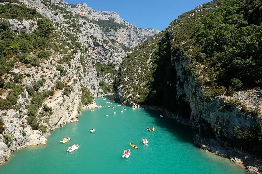 Vue horizontale depuis le pont du Galetas sur l'entrée des Gorges du Verdon avec de nombreux canoës et pédalos sur l'eau turquoise.