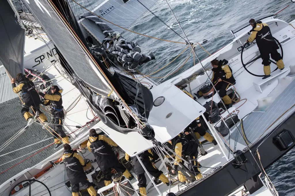Zoom aérien sur le cockpit du trimaran Spindrift 2 montrant l'équipage au travail et Yann Guichard à la barre dans une mer houleuse.