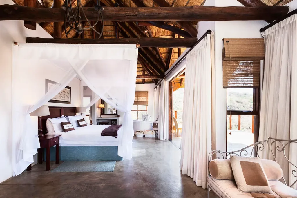 Intérieur d'une suite de luxe au Esiweni Luxury Safari Lodge avec lit à baldaquin et architecture traditionnelle en toit de chaume.