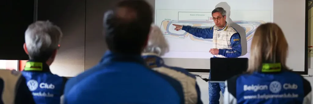 Jean-Marc Ponteville animant le briefing des pilotes devant une projection du tracé du circuit de Mettet.