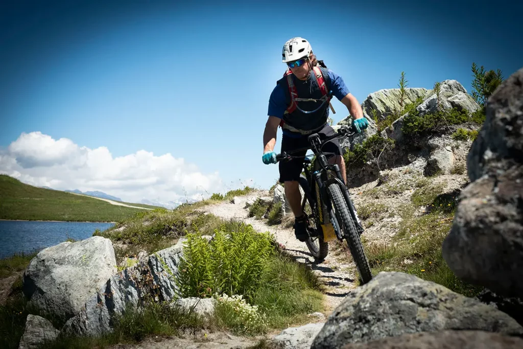 José Carron, guide et champion de VTT, roulant sur un sentier de montagne surplombant un lac d'altitude à Verbier.