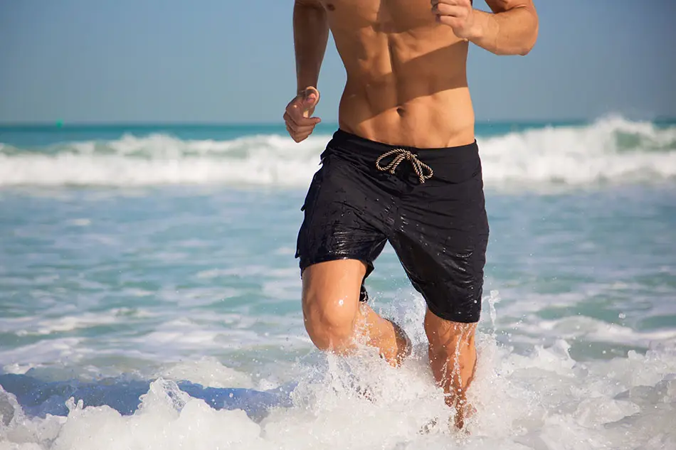 Homme courant dans les vagues avec un maillot Osseyan mouillé laissant deviner la forme d'un iPhone dans la poche étanche.
