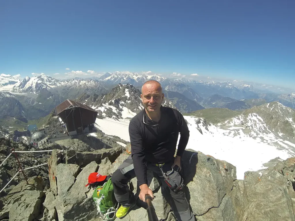 Le blogueur voyage Michel Gronemberger faisant un selfie GoPro au sommet du Mont-Fort (3330m) à Verbier, face au panorama des Alpes.