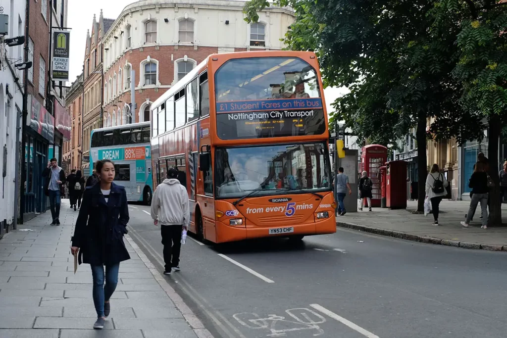 Place animée du centre-ville de Nottingham avec des passants et deux bus verts de la compagnie Nottingham City Transport.