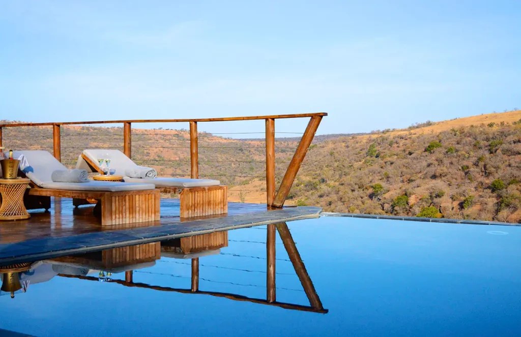 Piscine à débordement sur la terrasse en bois du Esiweni Luxury Safari Lodge avec vue sur la savane et champagne.