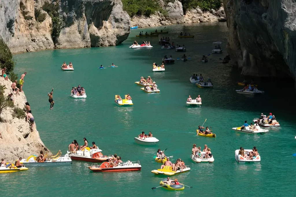 Photo horizontale au téléobjectif montrant des vacanciers plongeant depuis les falaises du Verdon entourés de pédalos.