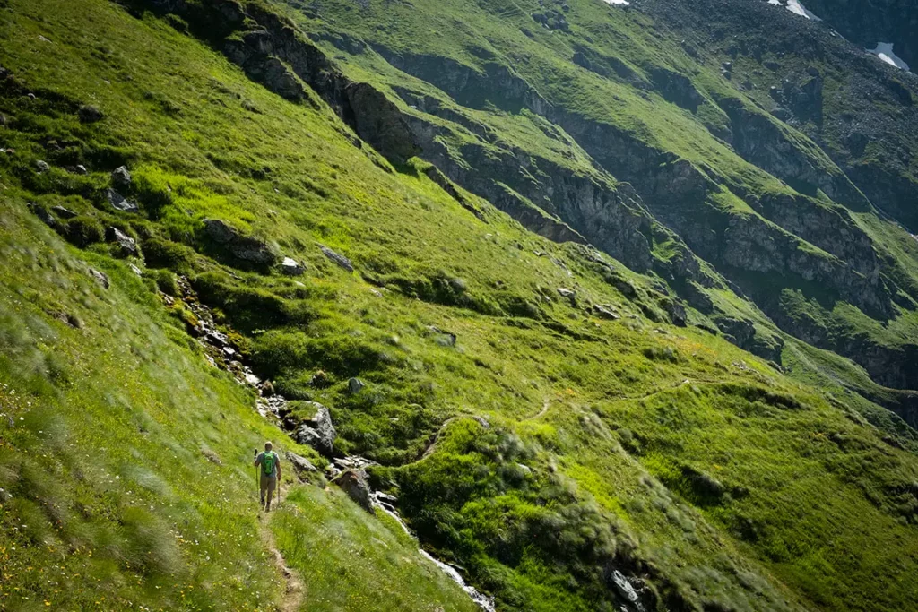 Randonneur marchant au début du Sentier des Chamois dans un paysage d'alpages verdoyants à flanc de montagne à Verbier en été.