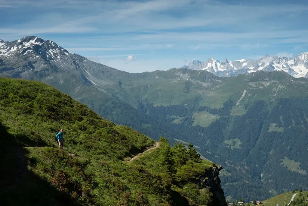 Un randonneur se reposant sur le Sentier des Chamois à Verbier en été, face à un panorama de montagnes enneigées et la vallée du Val de Bagnes.