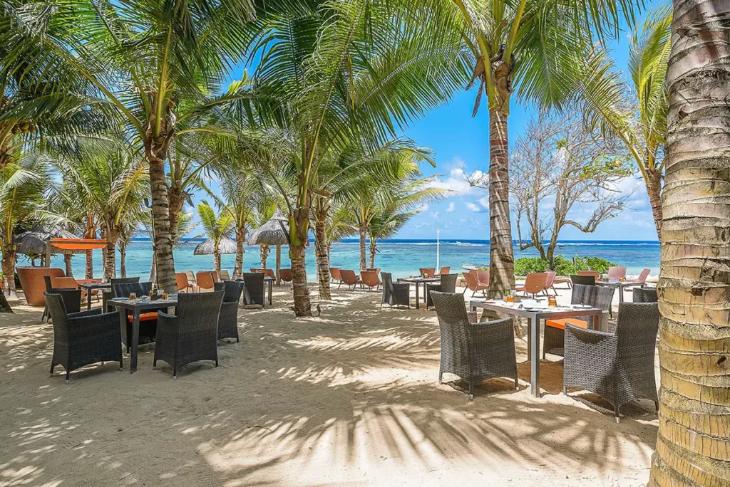 Tables du restaurant extérieur du So Sofitel Mauritius disposées sur le sable fin entre les palmiers face au lagon.