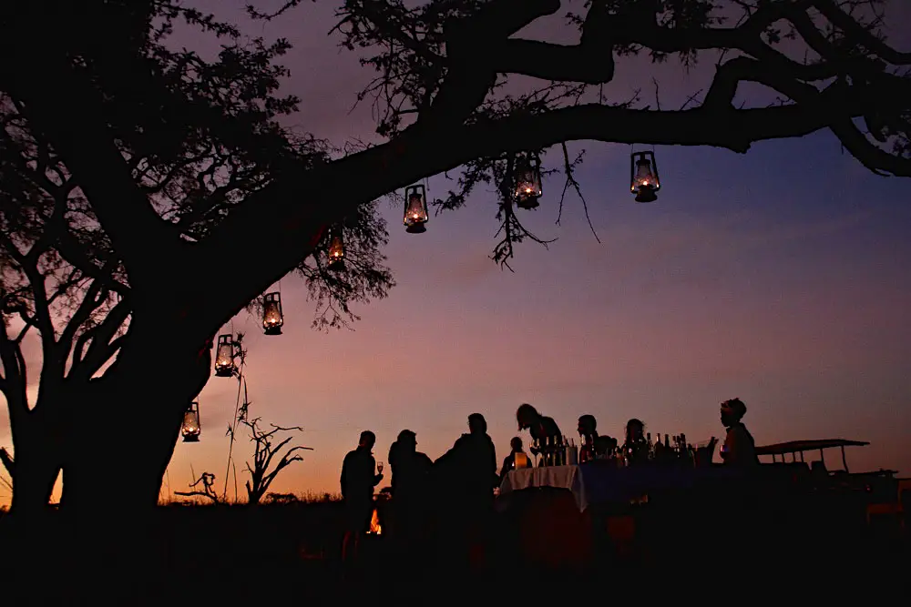 Silhouettes en ombres chinoises profitant du Sundowner au coucher du soleil au Esiweni Luxury Safari Lodge, éclairés par des lanternes.