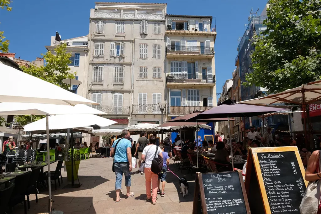 Terrasses ensoleillées et visiteurs sur la Place de Lenche lors d'une journée à Marseille.