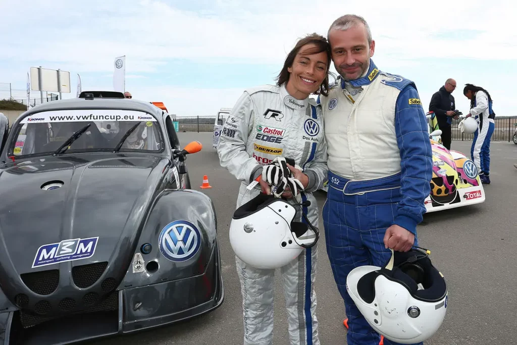 Vanina Ickx et Michel Gronemberger posant ensemble en combinaison de pilote devant des VW Fun Cup sur le circuit de Mettet.