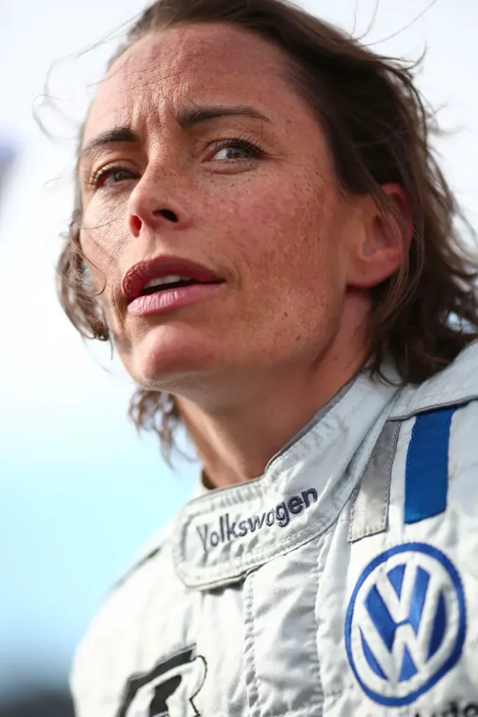 Portrait en contre-plongée de la pilote Vanina Ickx en combinaison de course Volkswagen avec logo au niveau du col.