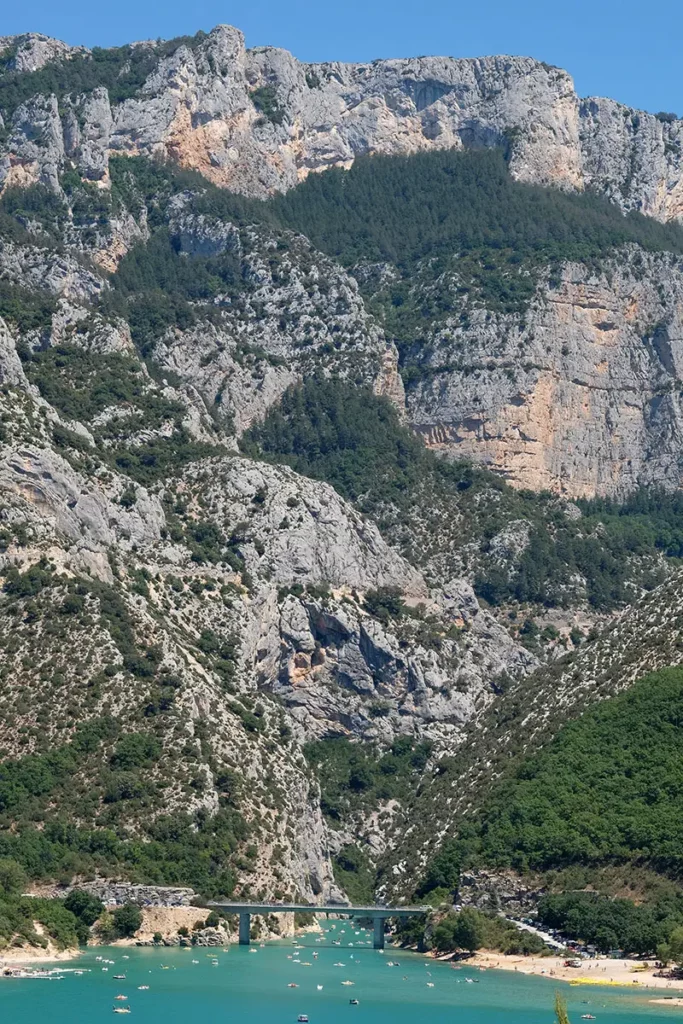 Photo verticale au téléobjectif montrant l'immensité des falaises des Gorges du Verdon surplombant le pont du Galetas et le bleu du lac.