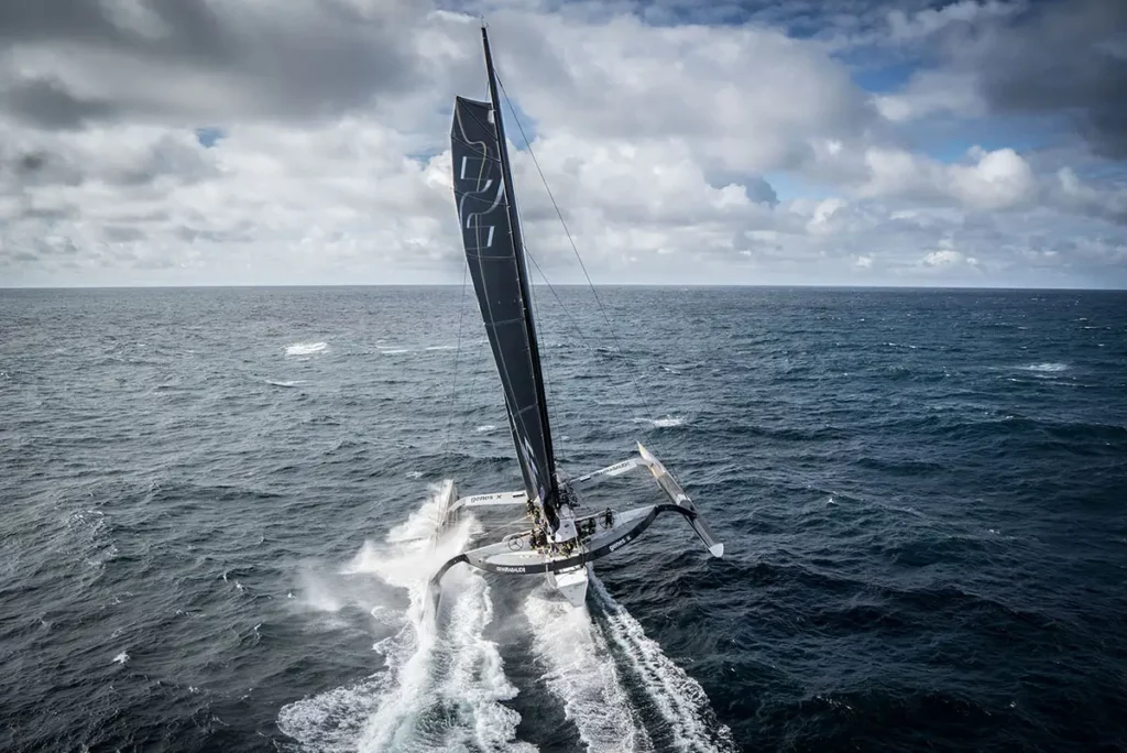 Vue aérienne arrière du trimaran Spindrift 2 montrant le sillage et l'écume générés par sa vitesse élevée sur l'océan.