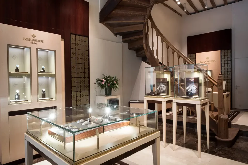Vitrines d'exposition Patek Philippe Genève chez la Maison De Greef à Bruxelles avec montres de luxe et escalier historique.