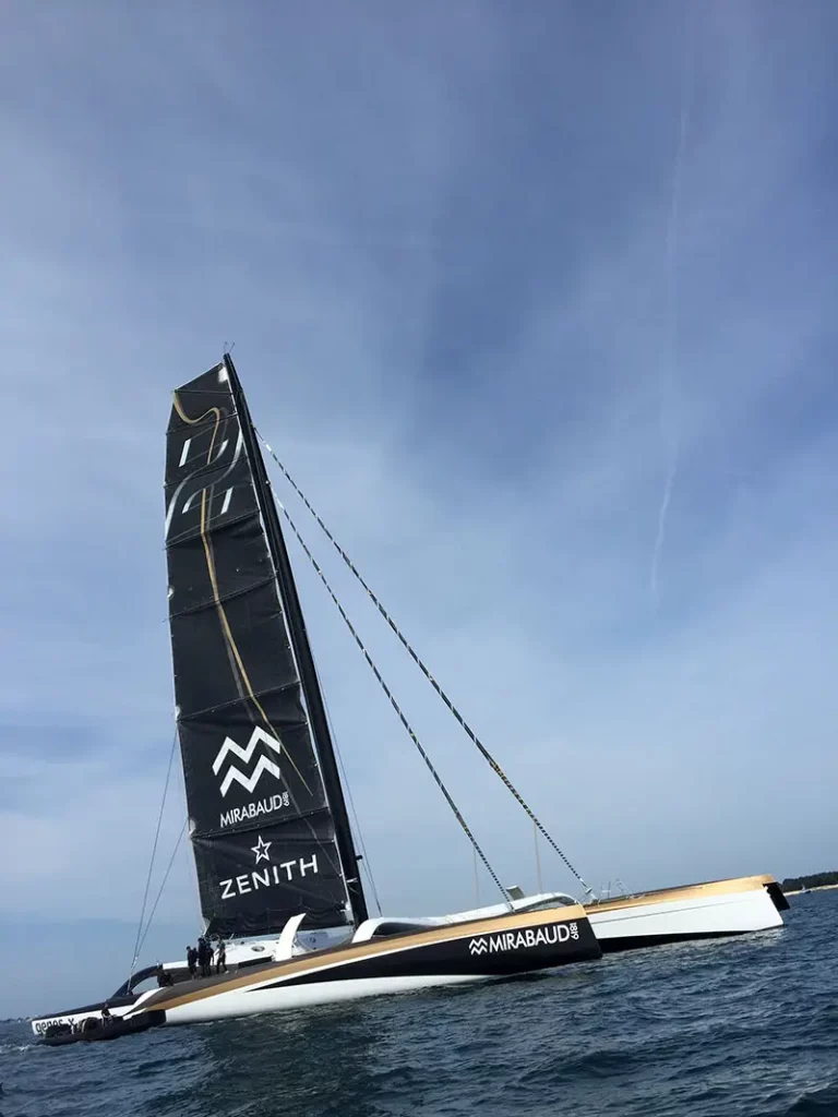 Vue en hauteur du trimaran Spindrift 2 avec la voile arborant le logo du sponsor Zenith Watches, prêt pour l'embarquement des partenaires.