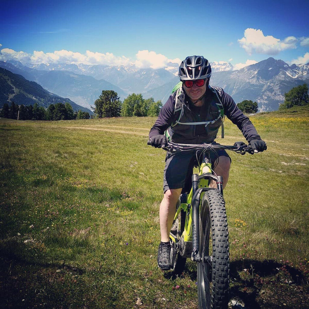 Le blogueur voyage Michel Gronemberger à Verbier en été souriant en VTT électrique sur un plateau d'alpage à Verbier, face aux montagnes.