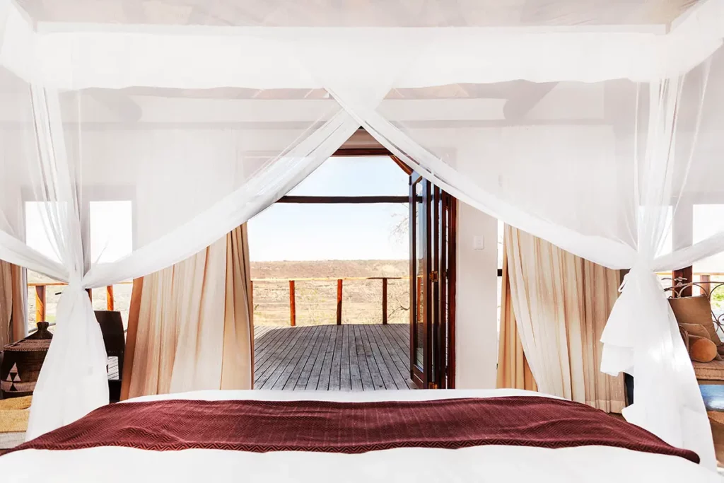 Vue sur la savane africaine depuis le lit à baldaquin d'une suite au Esiweni Luxury Safari Lodge.