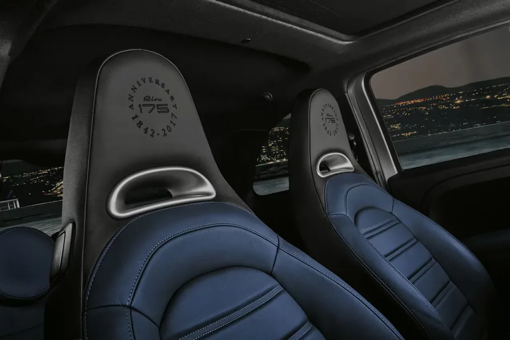 Détail de l'appuie-tête en cuir d'une Abarth 695 Rivale avec le logo brodé Riva 175 Anniversary 1842-2017 et lumières côtières en arrière-plan.