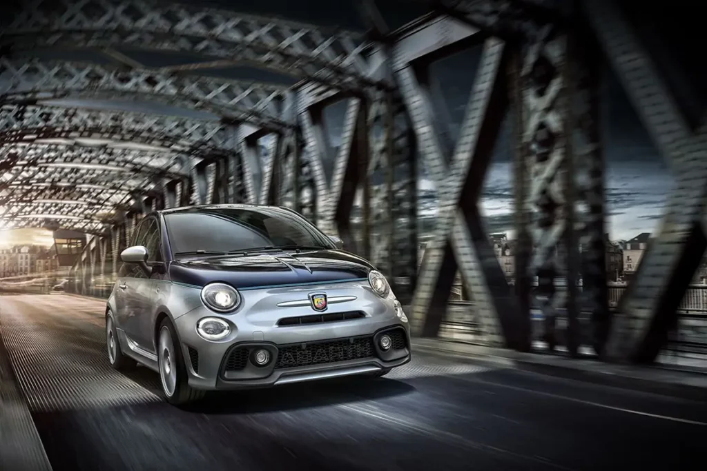 Effet de filé d'une Abarth 695 Rivale roulant à toute allure en vue 3/4 face sur un pont métallique riveté.
