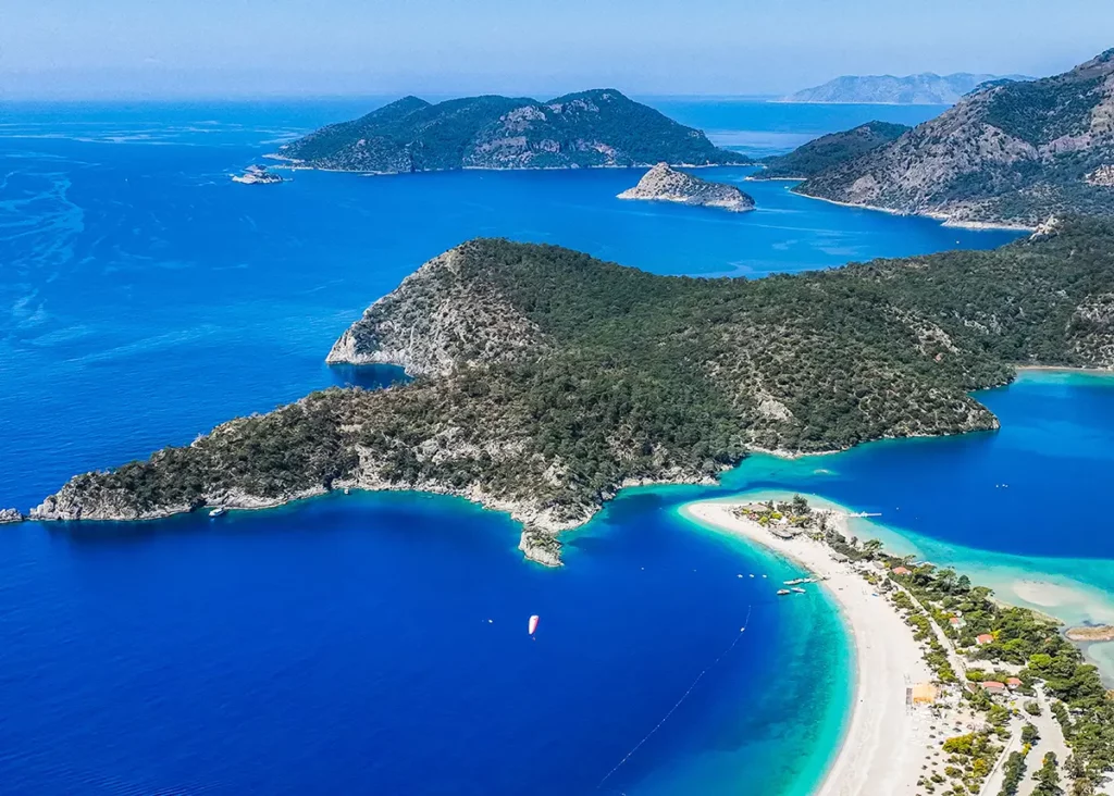 Vue panoramique de la baie d'Ölüdeniz à Fethiye, où les plages de sable blanc bordées d'un liseré turquoise dessinent des courbes au cœur des collines verdoyantes.