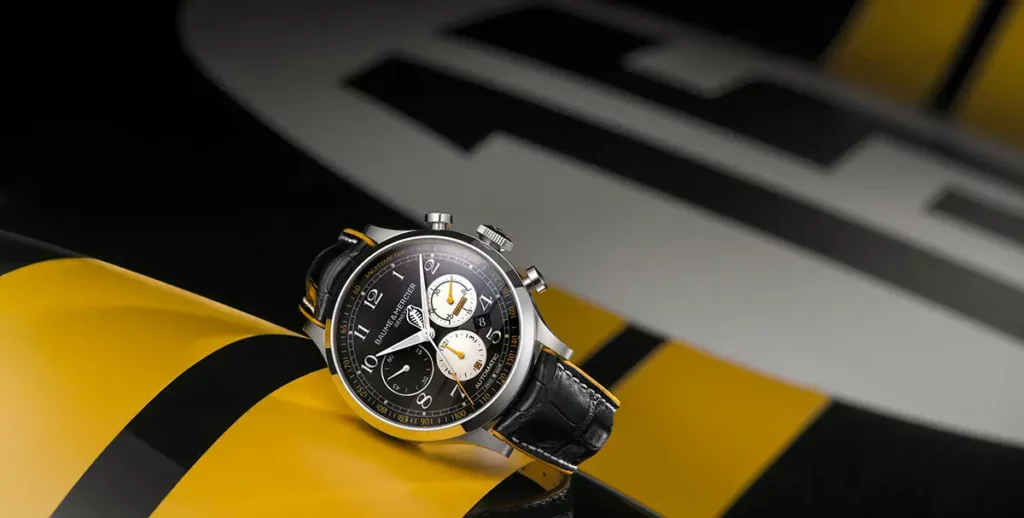 Photo de studio de la montre Baume & Mercier Capeland Shelby Cobra posée sur la carrosserie noire d'une Shelby Cobra. On voit le revers jaune du bracelet sur la bande jaune de la voiture, avec le numéro 15 blanc flouté en arrière-plan.