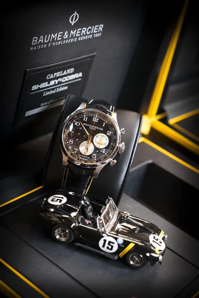 Photo verticale du coffret ouvert de la Baume & Mercier Capeland Shelby Cobra 1963 avec l'inscription de la marque visible, contenant la montre et le modèle réduit de la Shelby Cobra numéro 15.