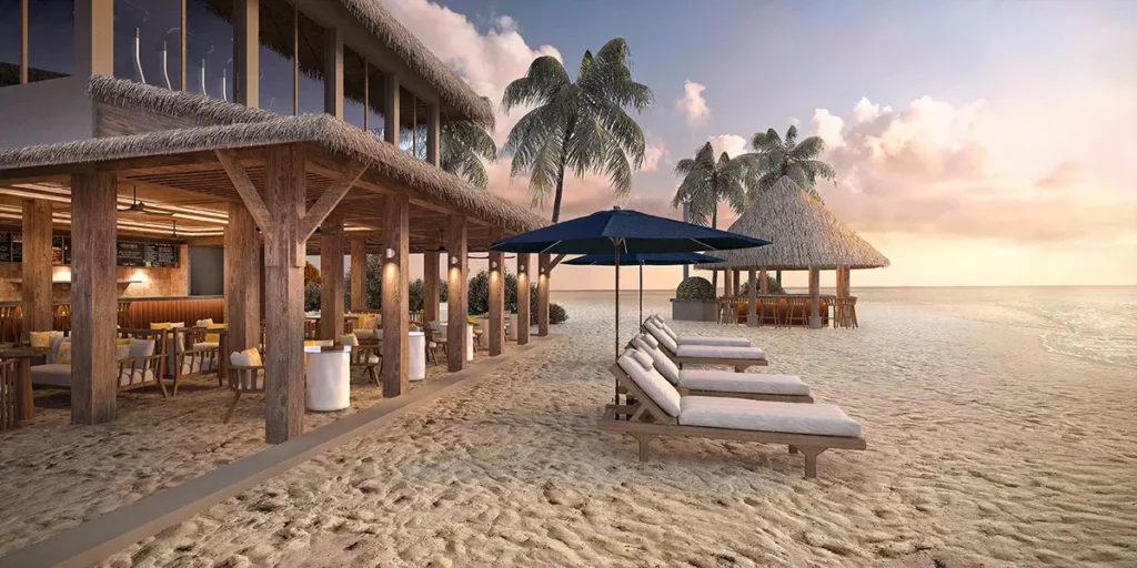 Vue de l'intérieur du restaurant Athiri à Emerald Faarufushi révélant ses imposantes poutres en bois face à la plage au coucher du soleil.