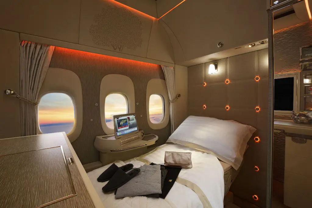 Suite de Première Classe Emirates en configuration lit avec hublots virtuels affichant un coucher de soleil.