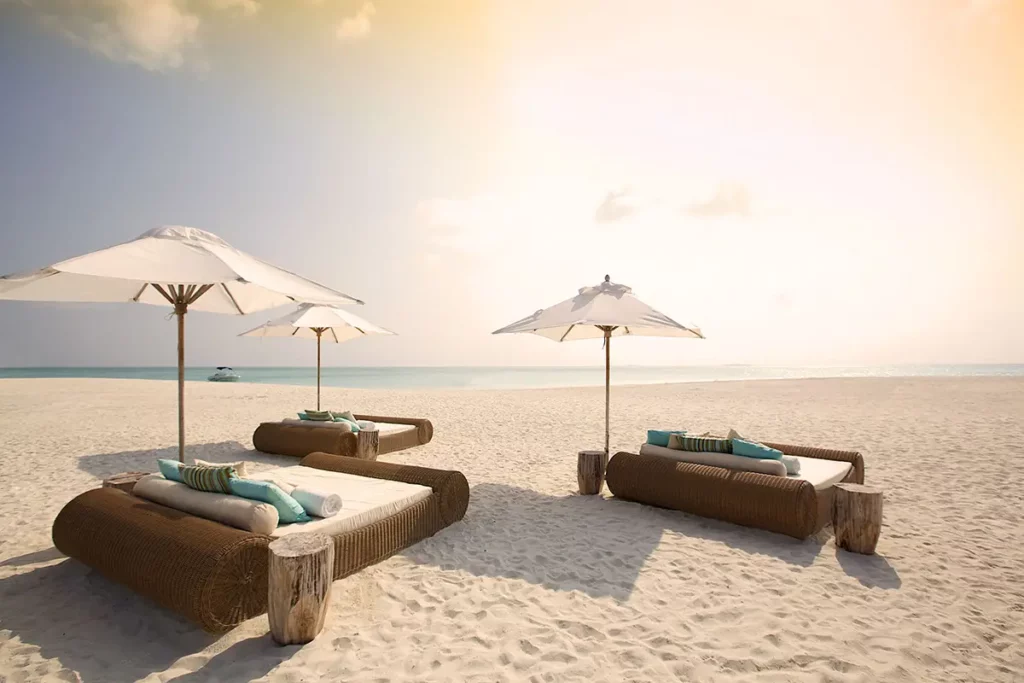 Trois fauteuils-lits avec parasols installés sur l'immensité de sable blanc face à la mer au Kanuhura.
