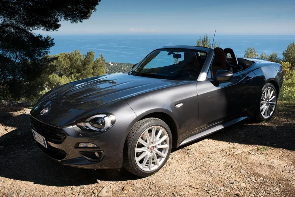 Fiat 124 Spider grise cabriolet garée sur une corniche ombragée face à la mer Méditerranée sur la route de Gorbio.