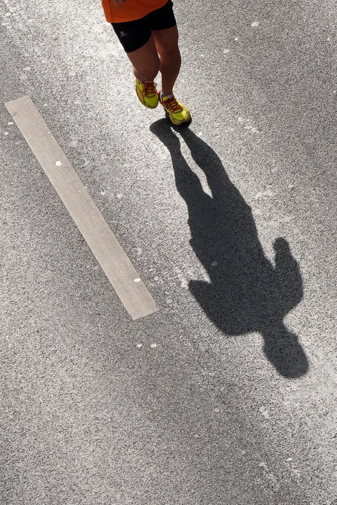 Vue verticale de l'ombre d'un joggeur et de ses deux pieds en pleine course sur l'asphalte des 20 km de Bruxelles.