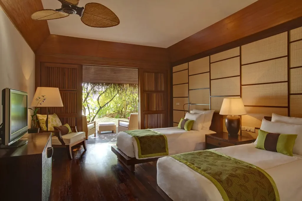 Chambre spacieuse d'une Grand Beach Villa au Kanuhura avec deux lits simples et vue sur la végétation tropicale.