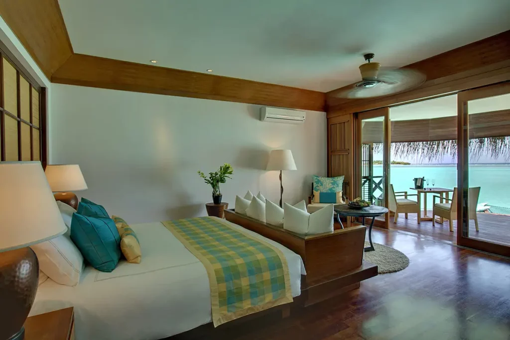 Chambre de Water Villa au Kanuhura avec vue sur le lagon depuis la baie vitrée et l'échelle d'accès à l'eau.