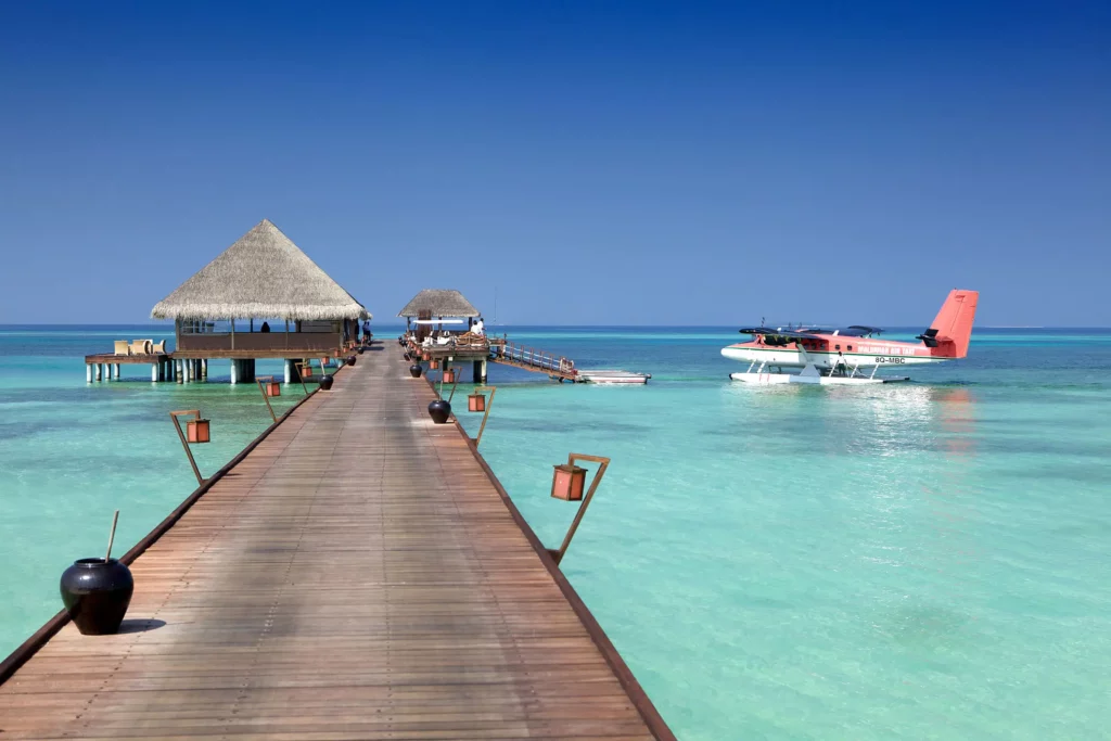 Vue de la jetée en bois de l'hôtel Kanuhura aux Maldives avec un hydravion Maldivian Air Taxi amarré au ponton d'accueil.