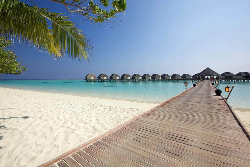 Départ de la jetée en bois sur le sable blanc menant aux Water Villas sur pilotis du Six Senses Kanuhura au-dessus du lagon turquoise.