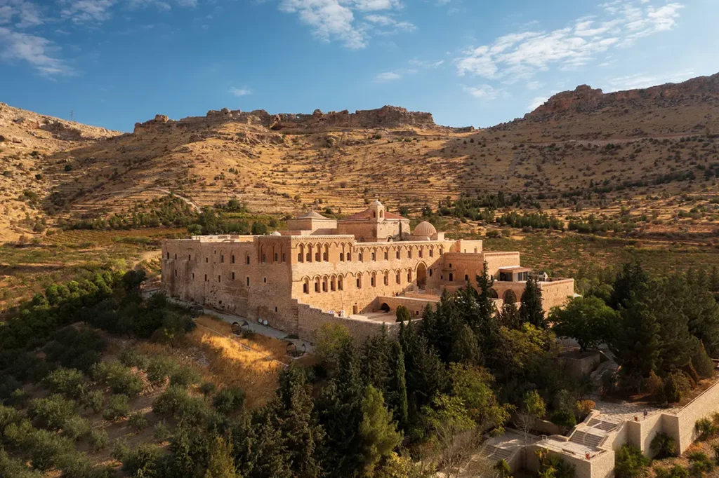 Monastère de Deyrülzafaran à Mardin, construit en pierres locales de couleur ocre se fondant dans le paysage de montagnes et de végétation environnant.