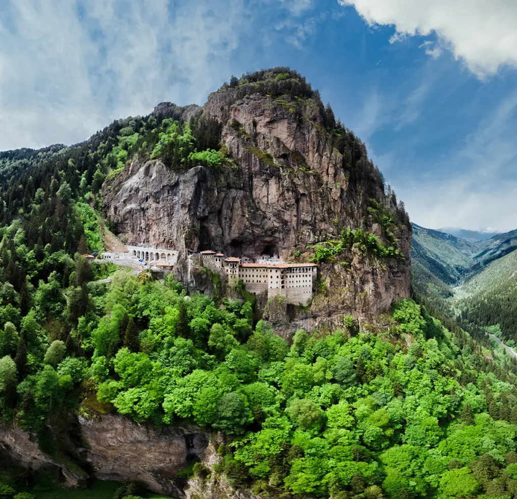 Vue aérienne du monastère de Sumela perché à flanc de falaise contre la montagne à Trabzon, surplombant une dense végétation qui masque le bas de la vallée.