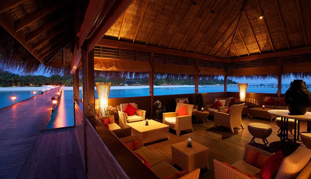 Vue nocturne du Moodhu Lounge au Kanuhura avec la jetée illuminée menant vers l'île principale aux Maldives.
