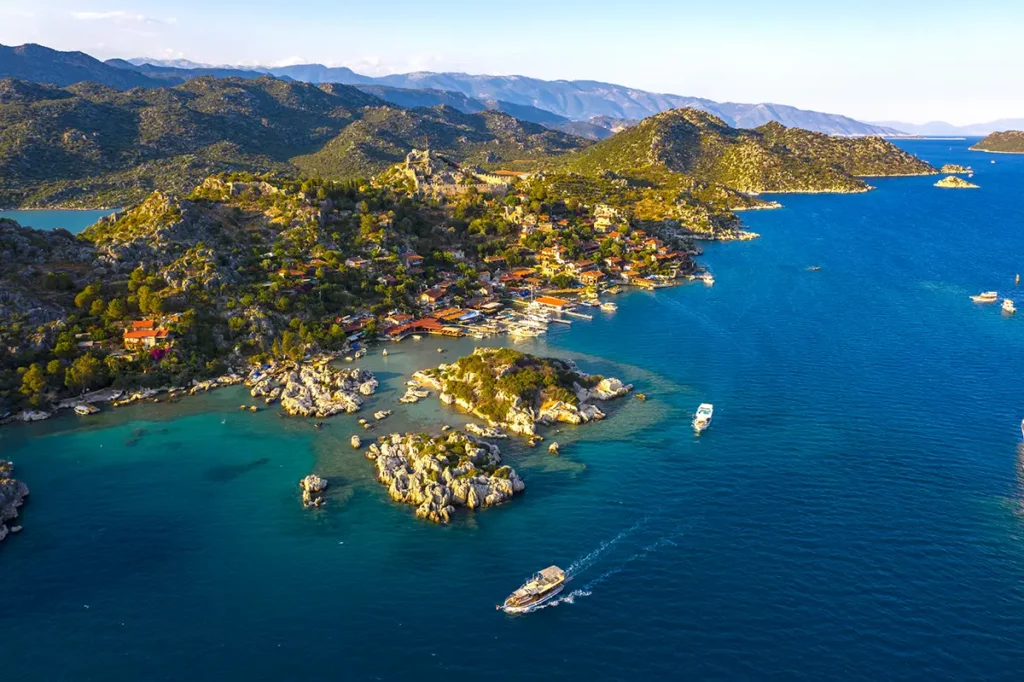 Paysage côtier accidenté à Kale Üçağız dans la région d'Antalya, montrant des rochers escarpés, de la végétation méditerranéenne, des criques sauvages et des bateaux locaux sur l'eau bleue.