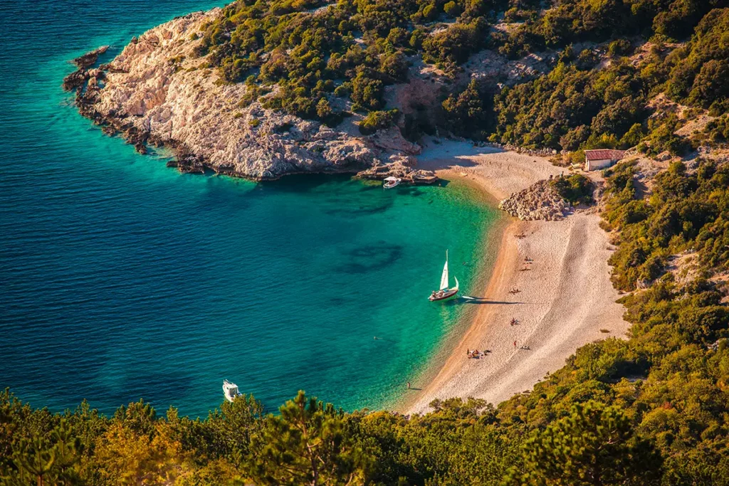 Vue en plongée de la plage de Lubenice sur l'île de Cres sous une lumière dorée, un paysage de carte postale emblématique des îles croates.