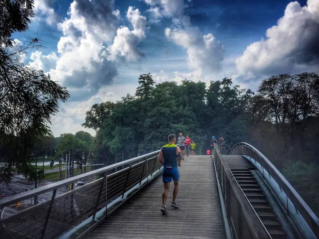 Passerelle en bois de la Promenade Verte enjambant l'avenue de Tervueren au niveau du Musée du Tram à Woluwe, avec des promeneurs et joggeurs.