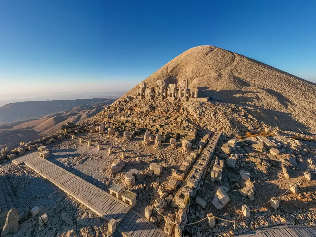 Vue aérienne du site archéologique du mont Nemrut en Turquie au lever du soleil, montrant les statues antiques assises sans leurs têtes face aux montagnes.