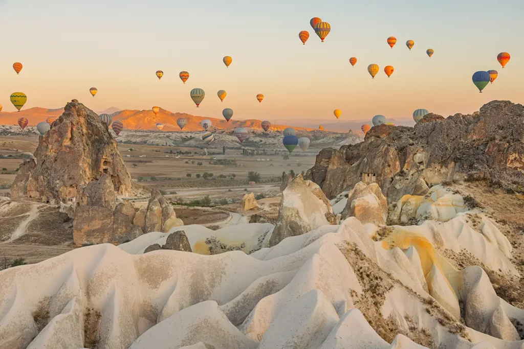 Vol de montgolfières au lever du soleil en Cappadoce au-dessus des cheminées de fées et des collines en dégradé d'ocre et de brun, lors d'un road-trip en Turquie.