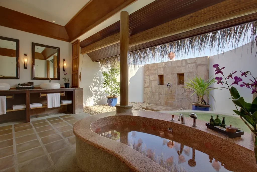 Salle de bain d'une villa sur pilotis au Kanuhura avec baignoire et douche extérieure à ciel ouvert.