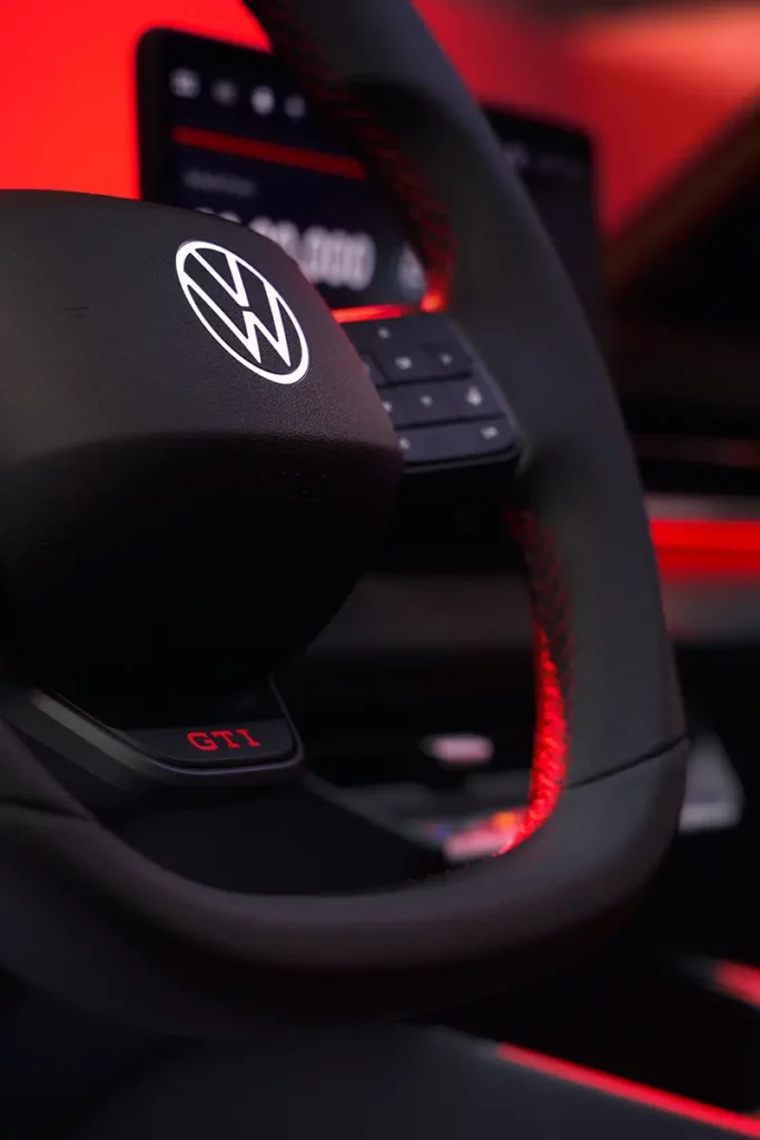 Gros plan sur le volant sport d'une Volkswagen ID. Polo GTI électrique avec logo VW rétroéclairé, logo GTI rouge vif lumineux à 6 heures et ambiance rouge.